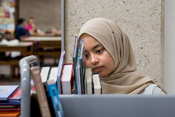 Student looks closely at top of bookshelf.
