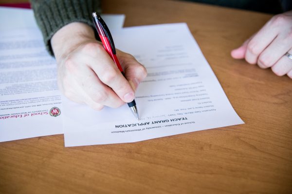 Close up of hands writing on a paper atop wooden table.