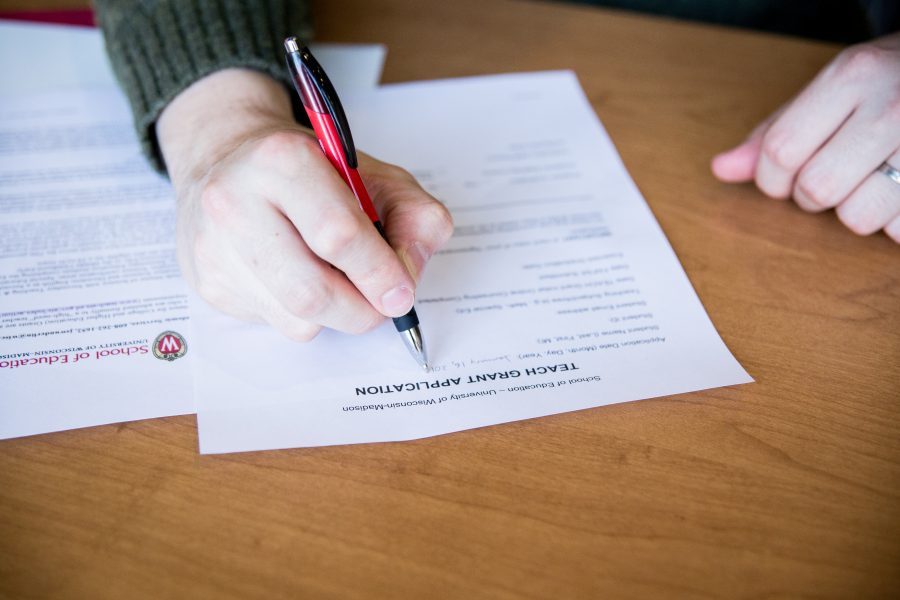 Close up of hands writing on a paper atop wooden table.