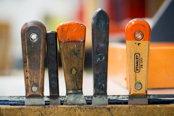 Handles of five varying art tools sticking out of a wooden drawer.