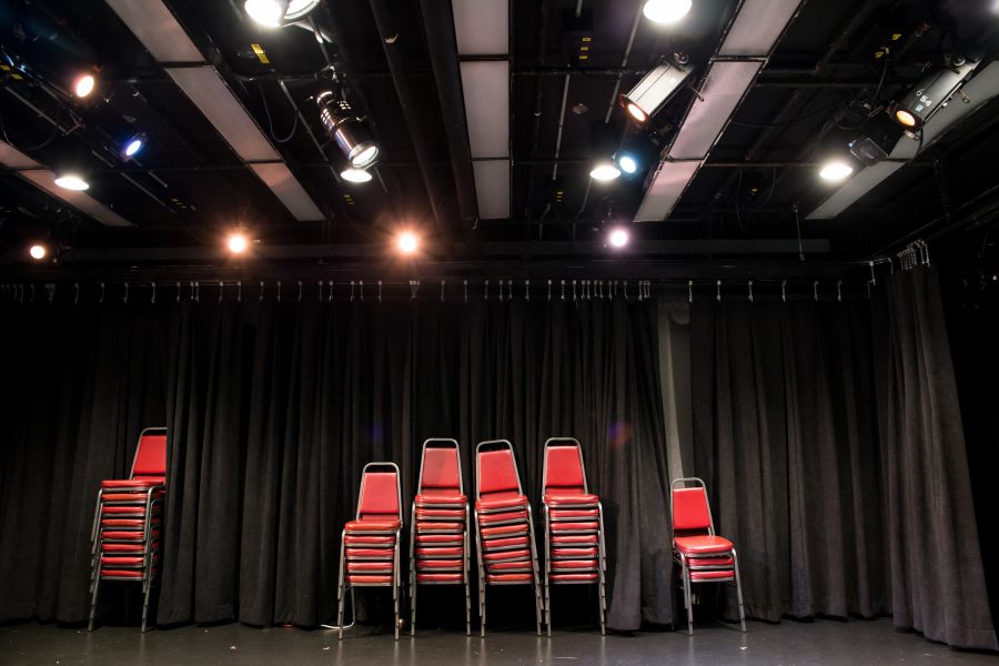 Red chairs stacked on each other in front of black curtain.