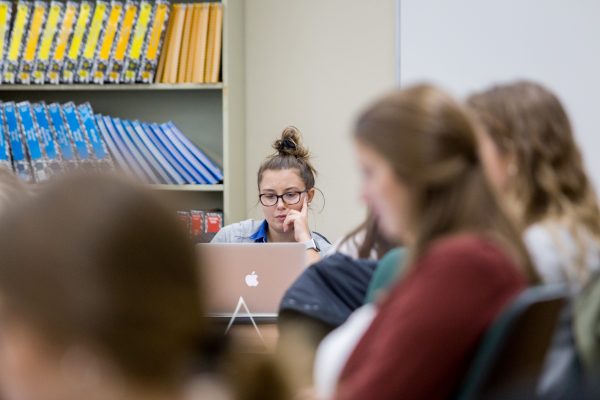 Three students frame the image as it focuses on a singular female student studying on her laptop.