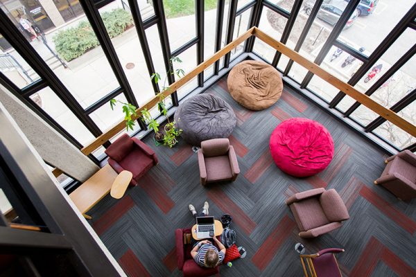 Bird's eye view of student sitting on and surrounded by varying chairs in Merit Library.