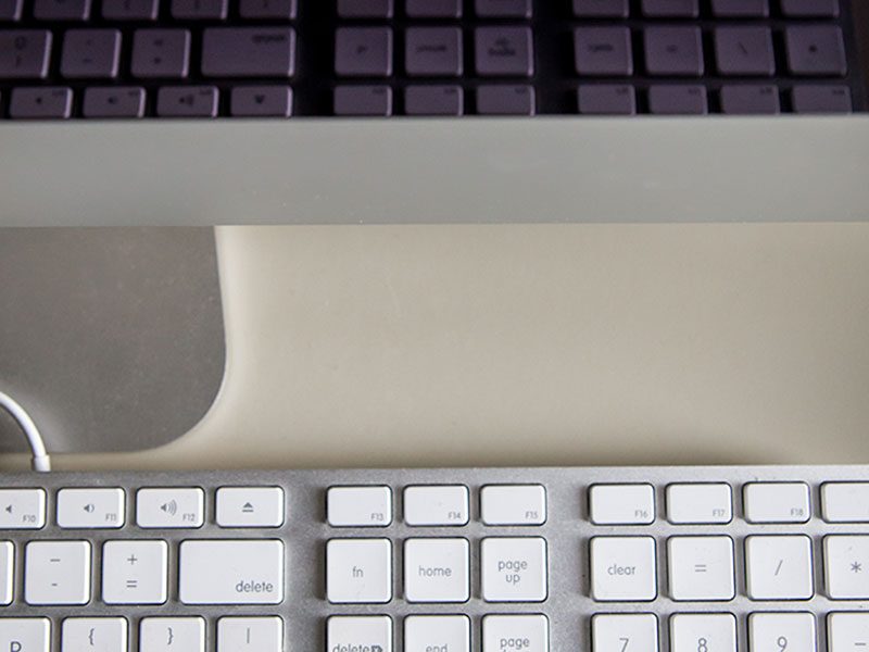 A close up of the bottom of a MAC screen and the top of a white keyboard.