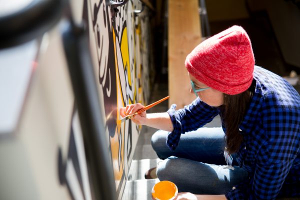 Student with red beanie using yellow paint on wall.