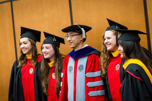 Five graduating students looking away and smiling as they get their pictures taken.