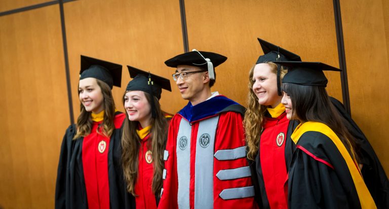 Five graduating students looking away and smiling as they get their pictures taken.