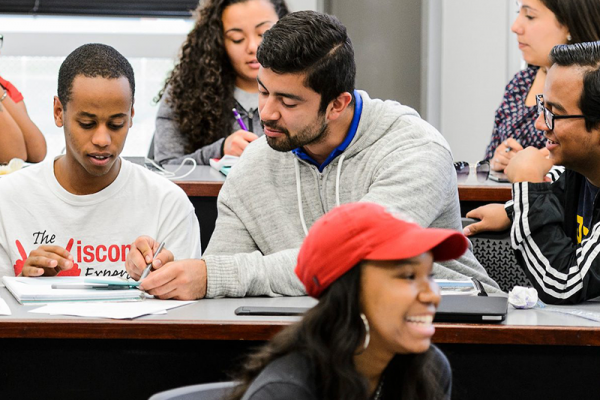 Students leaning over laughing and talking as they do their work.