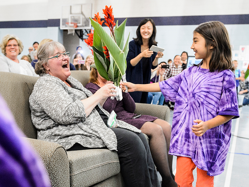 Little girl in purple tie dye shirt giving older lady flowers.