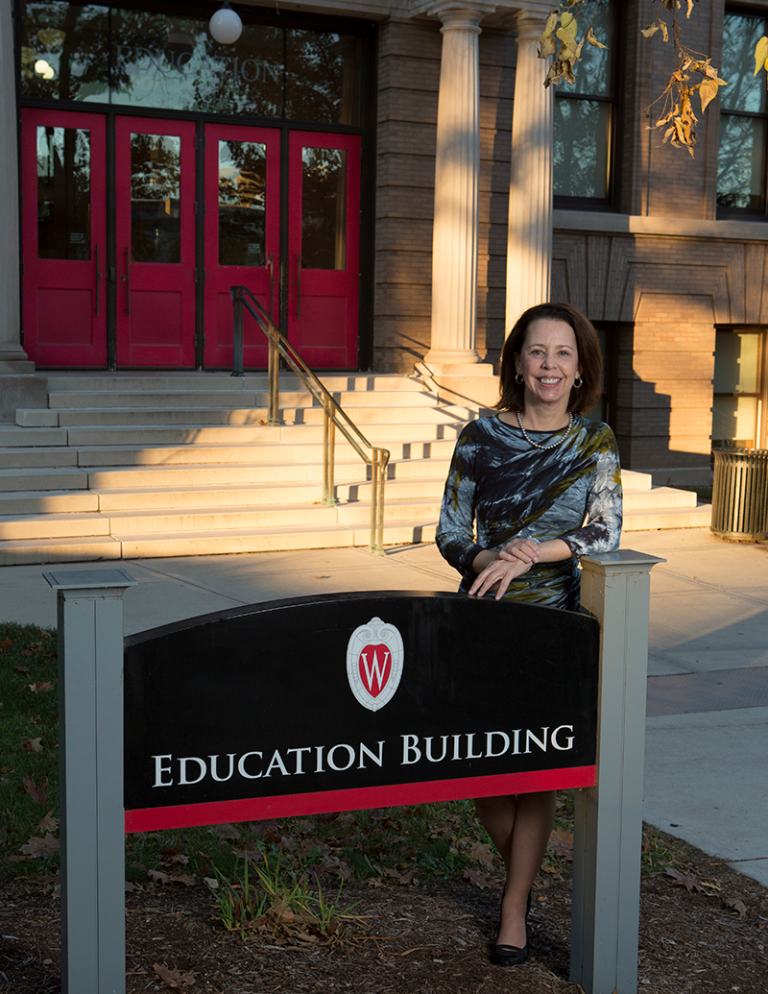 Dean Diana Hess smiling and standing behind Education Building sign.