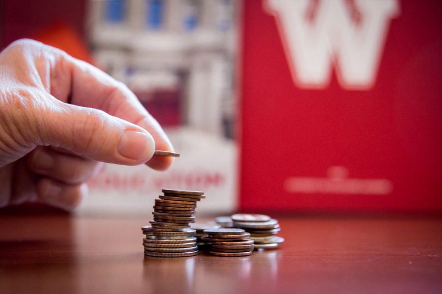 A hand reaching out from the left side stacking a pile of coins on each other.