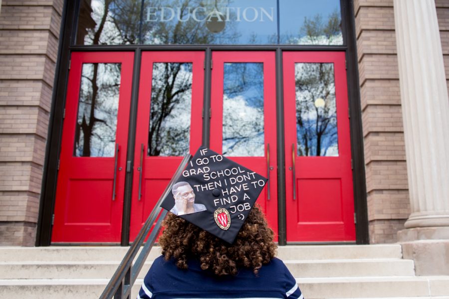 Graduate standing in front of the red doors of the Education building.